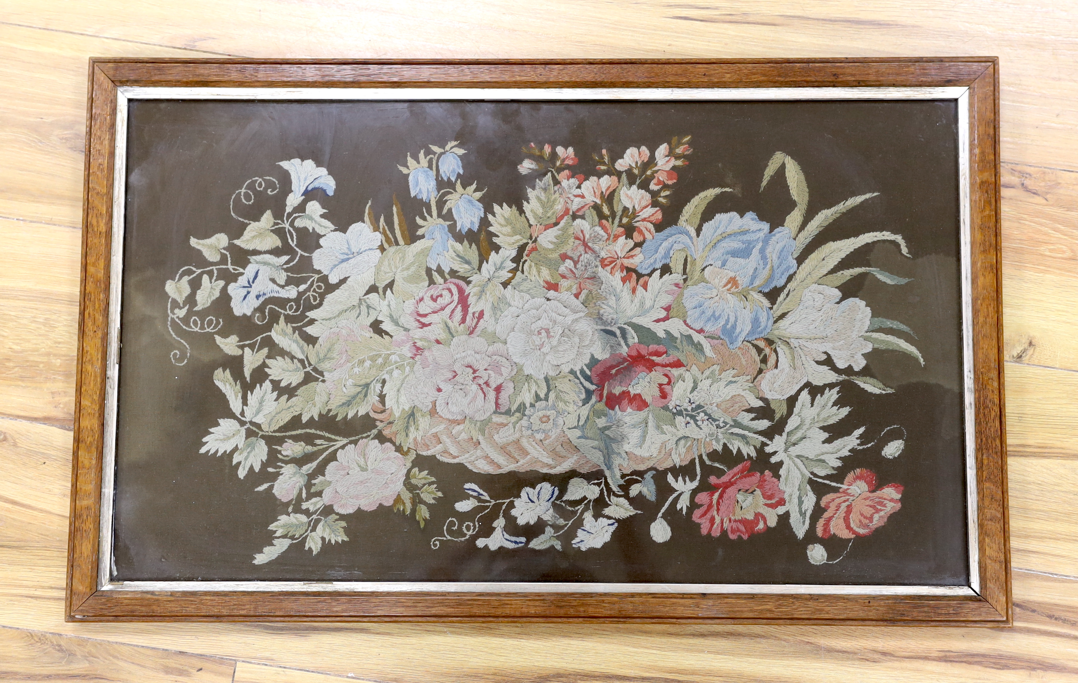 A 19th century framed floral needlework embroidery of a basket of flowers. Worked in multi coloured silks on a felt background, 65cm wide x 38cm high